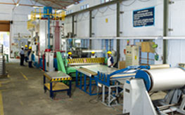 A production hall with a steel coil line and workers in hard hats.