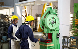 Two workers in hard hats and aprons at a green power press.